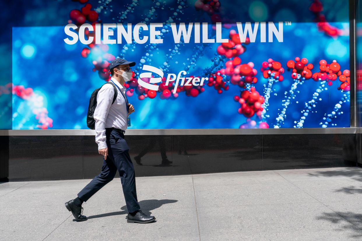 A pedestrian wearing a face mask walks past a sign hanging outside Pfizer headquarters in Manhattan, New York, Monday, May 23, 2022. 