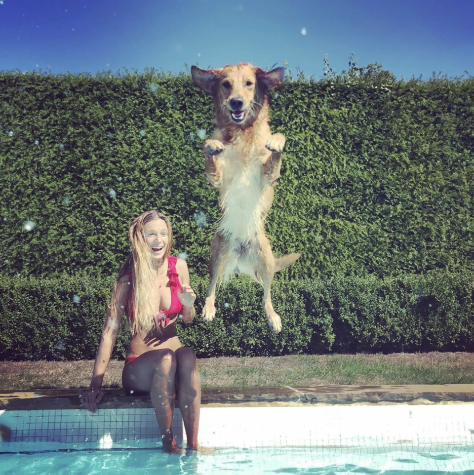 A photo of Alizée Thevenet wearing a red bikini sitting on the side of a pool as a dog leaps into the water