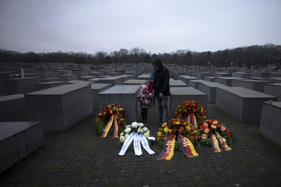 A father with his two kids stay behine wreaths, placed at the Memorial to the Murdered Jews of Europe on the International Holocaust Remembrance Day in Berlin, Germany, Friday, Jan. 27, 2023. (AP Photo/Markus Schreiber)