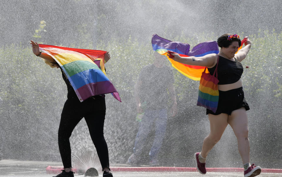 A women with a rainbow flag cools off in a sprinkler ahead of the Equality Parade, the largest LGBT pride parade in Central and Eastern Europe, in Warsaw, Poland, Saturday, June 19, 2021.(AP Photo/Czarek Sokolowski)