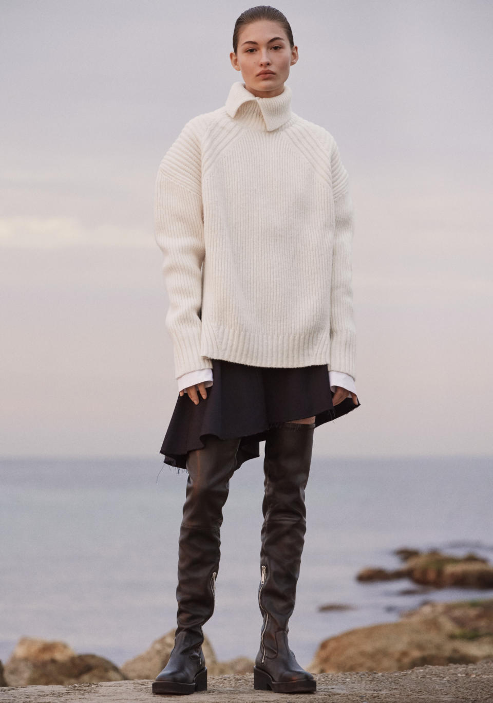 Model Grace Elizabeth in a ribbed turtleneck, an asymmetrical skirt, and thigh-high boots from H&M Studio AW17, photographed by Christian MacDonald, styled by Ludivine Poiblanc, in Mallorca, Spain. (Photo: Courtesy of H&M)