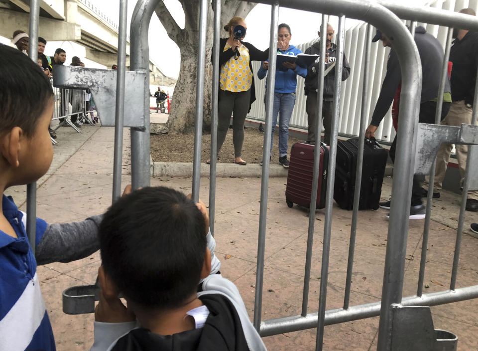 FILE - In this Thursday, Sept. 26, 2019 file photo, Two Mexican boys in Tijuana, Mexico, listen to volunteers calling names from a waiting list to claim asylum in the U.S. at a border crossing in San Diego. A federal judge ruled Thursday, Sept. 2, 2021 that the U.S. government's practice of denying migrants a chance to apply for asylum on the Mexican border until space opens up to process claims is unconstitutional.(AP Photo/Elliot Spagat, File)