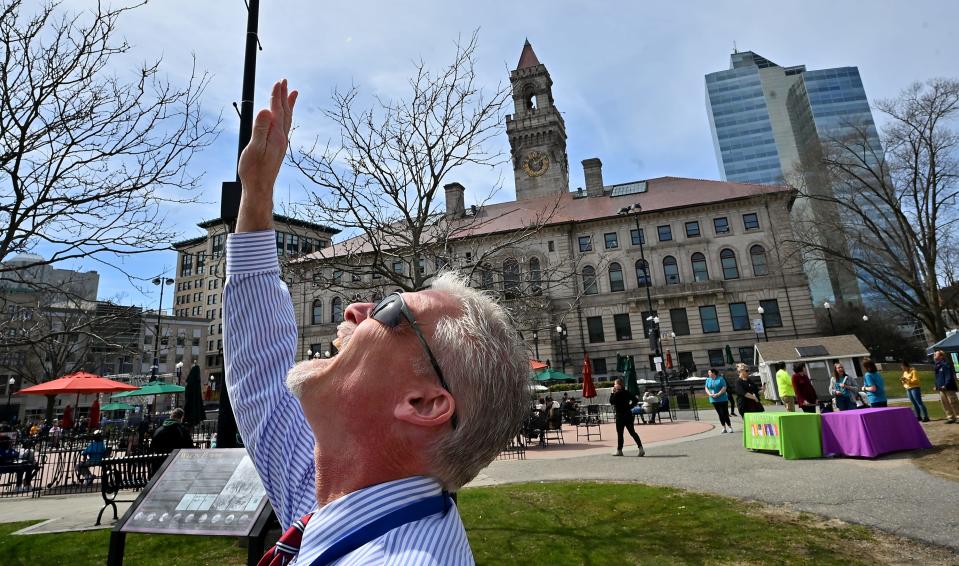 Douglas Lord, a director of library services at the Worcester Public Library, uses his hand to block to sun while monitoring a long line to get eclipse-viewing glasses on the Worcester Common.