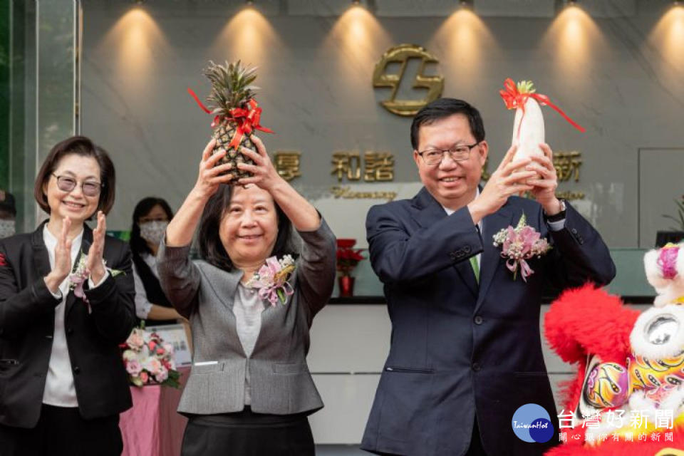 鄭市長與土地銀行董事長謝娟娟手持蘿蔔及鳳梨，祝福青埔分行業績長紅