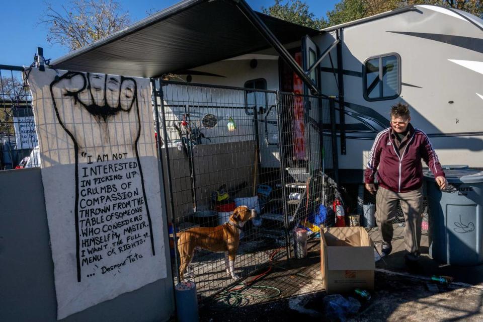 Joyce Williams goes about her morning chores Wednesday, Dec. 13, 2023, near her trailer as one of her dogs Archie looks on from his pen inside Camp Resolution in North Sacramento. “For a year no one has been swept in this camp. They haven’t had that stress on them. It’s overwhelming the preparations for a sweep,” said Williams.