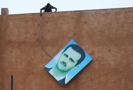 A member of al Qaeda's Nusra Front takes down a picture of Syria's President Bashar al-Assad in the northwestern city of Ariha, after a coalition of insurgent groups seized the area in Idlib province May 29, 2015. REUTERS/Ammar Abdullah