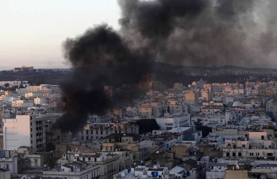 FILE - In this file photo dated Friday, Jan. 14, 2011, a column of smoke rises from buildings during clashes between protesters and police in Tunis. Tunisia's president declared a state of emergency and announced that he would fire his government as violent protests escalated Friday, with gunfire echoing in the North African country's usually calm capital and police lobbing tear gas at protesters. On Thursday Jan. 14, 2021, Tunisia commemorates 10 years since the flight into exile of its iron-fisted leader, Zine El Abidine Ben Ali, pushed from power in a popular revolt that foreshadowed the so-called Arab Spring.(AP Photo/Christophe Ena)