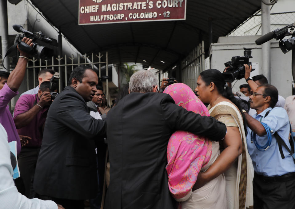 Sri Lankan Swiss embassy worker Garnier Banister Francis, covered in pink shawl, holds on to an unidentified foreign national as Sri Lankan police officers escort her to a magistrate court after her arrest in Colombo, Sri Lanka, Monday, Dec. 16, 2019. (AP Photo/Eranga Jayawardena)