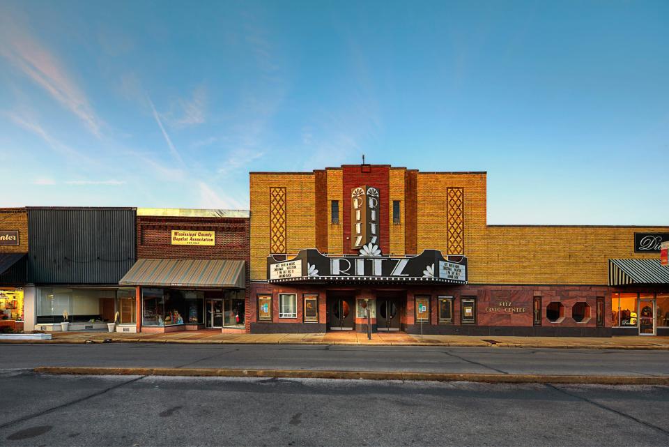 A shot of a street in Blytheville, Arkansas, with the Ritz civic center, which has an Art Deco-style marquee, at the center. Also visible are other storefronts, most with brick facades.