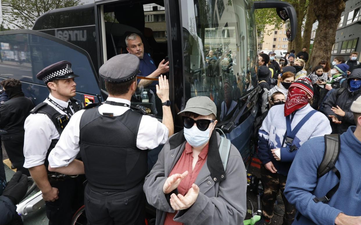 Police officers speak to the bus driver as protesters surround the vehicle