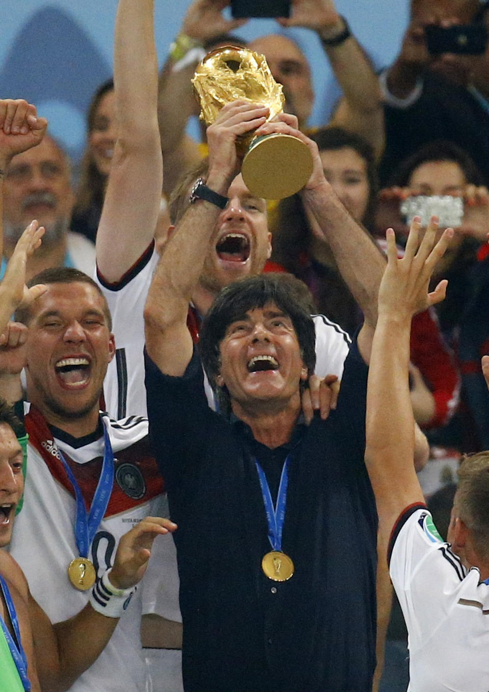 Germany's coach Joachim Loew lifts the World Cup trophy next to Lukas Podolski (L) after the 2014 World Cup final between Germany and Argentina at the Maracana stadium in Rio de Janeiro July 13, 2014. REUTERS/Kai Pfaffenbach (BRAZIL - Tags: SPORT SOCCER WORLD CUP TPX IMAGES OF THE DAY)