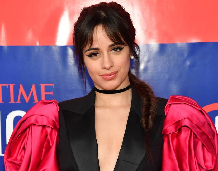Camila wears a black dress with plunging neckline and red poofy sleeves