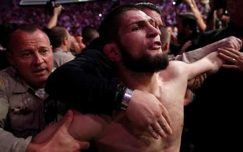 Khabib Nurmagomedov is restrained after plunging out of the cage and into the crowd - Credit: John Locher/AP