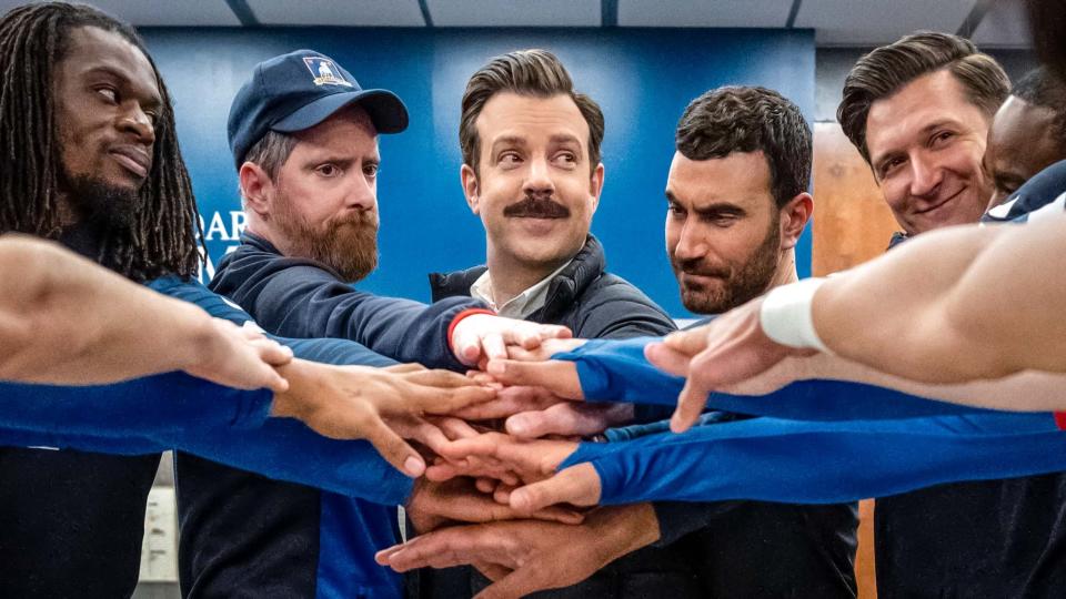 (L to R) Brendan Hunt as Coach Beard, Jason Sudeikis as Ted Lasso and Brett Goldstein as Roy Kent putting their hands in the middle before a game in Ted Lasso season 3 episode 12, 