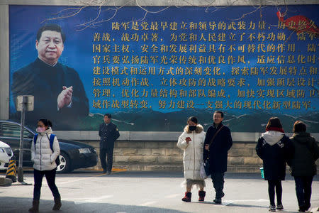 FILE PHOTO: People walk in front of a poster showing a portrait of Chinese President Xi Jinping in Beijing, China, February 26, 2018. REUTERS/Thomas Peter/File Photo