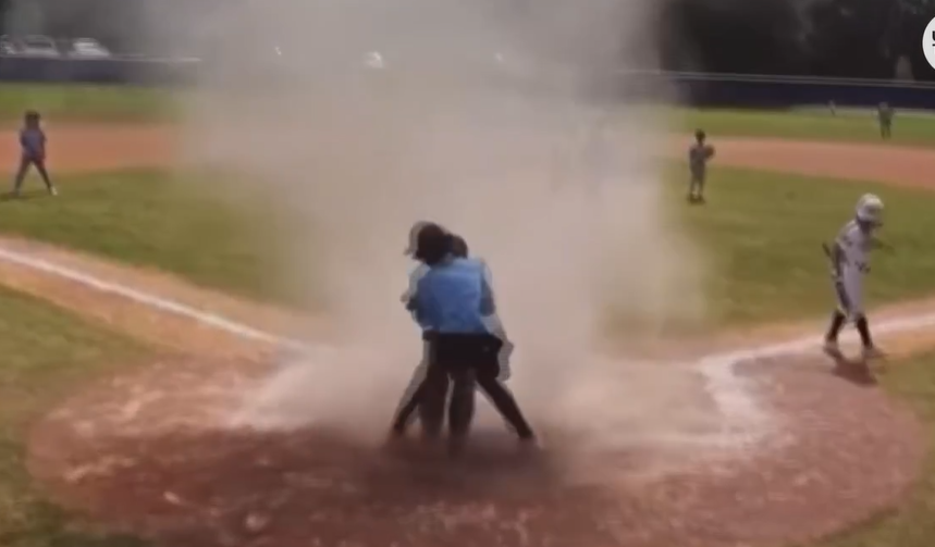 This video image shows umpire Aidan Wiles lifting catcher Bauer Zoya out of a dust devil during a youth baseball game Sunday in Jacksonville.