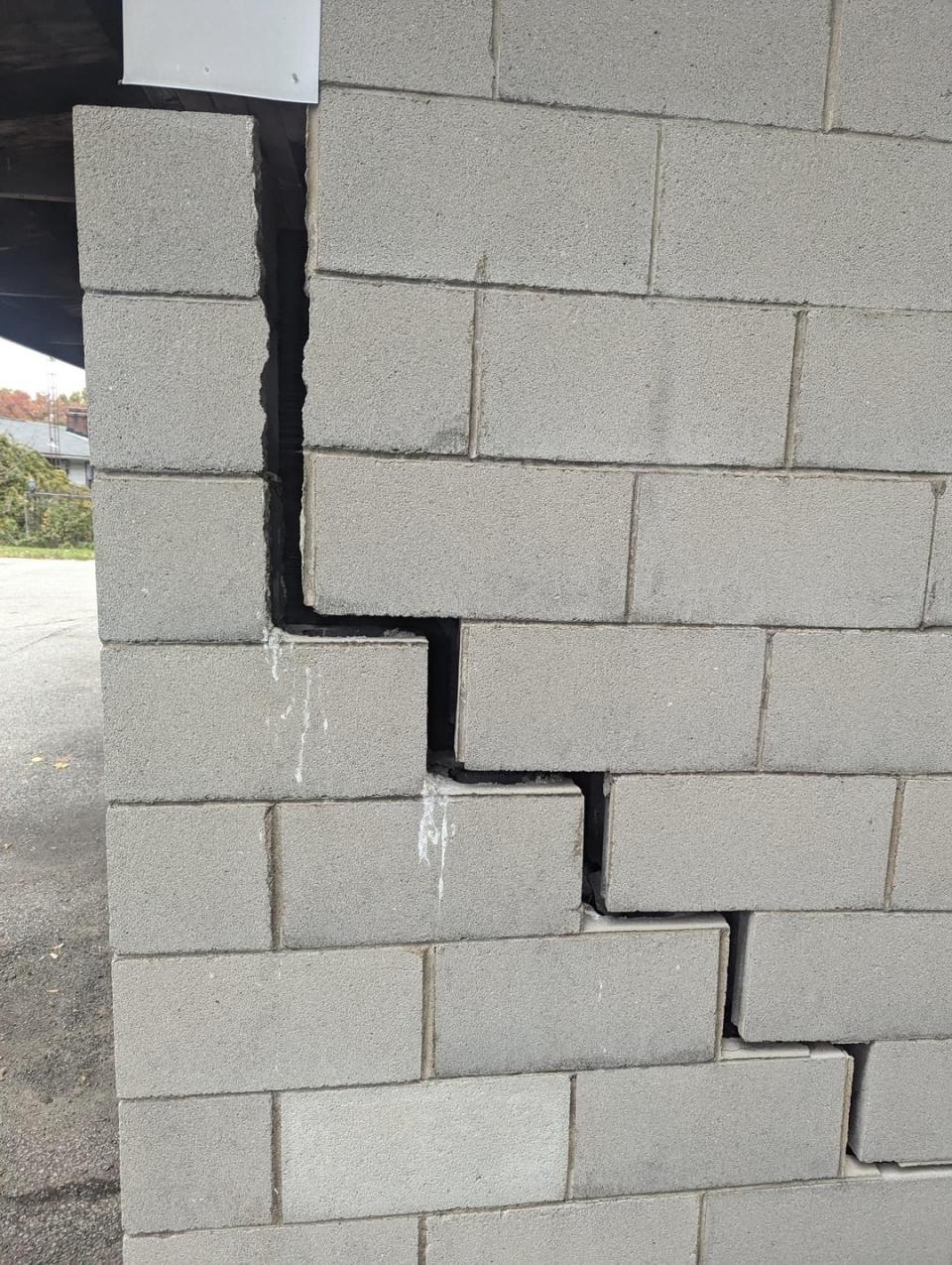 A cinder block wall showing signs of structural failure with a visible large crack and shifted bricks