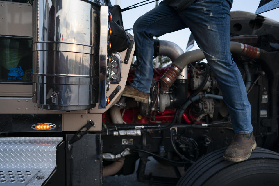 In this April 5, 2020, photo, trucker Sammy Lloyd, of Ringgold, Ga., stands of the tire his 2014 Kenworth W900 semitruck to wash the windshield during a fuel stop at the Fas Mart in Winchester, Ky. Lloyd is pulling a COVID-19 emergency relief load from California to Virginia. (AP Photo/Carolyn Kaster)