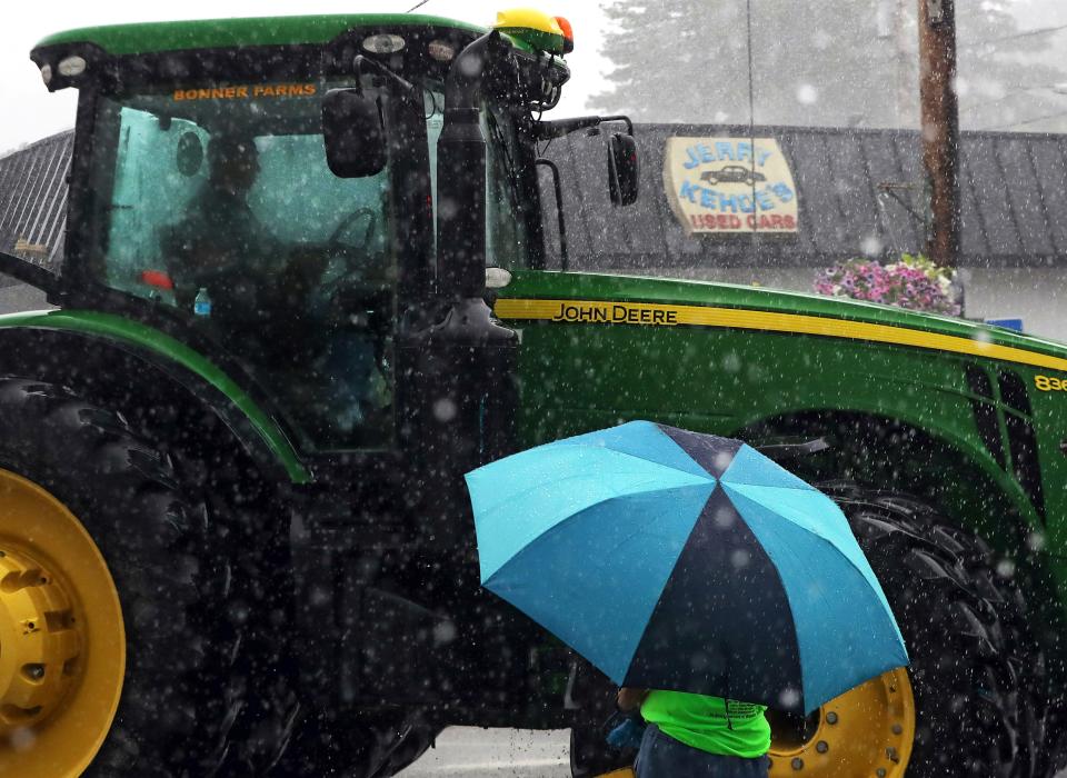 The driver of a John Deere from Bonner Farms stays dry in his enclosed cab as a spectator tries to stay dry under an umbrella during the Garrettsville Tractor Parade, Saturday, June 29, 2024, in Garrettsville, Ohio.