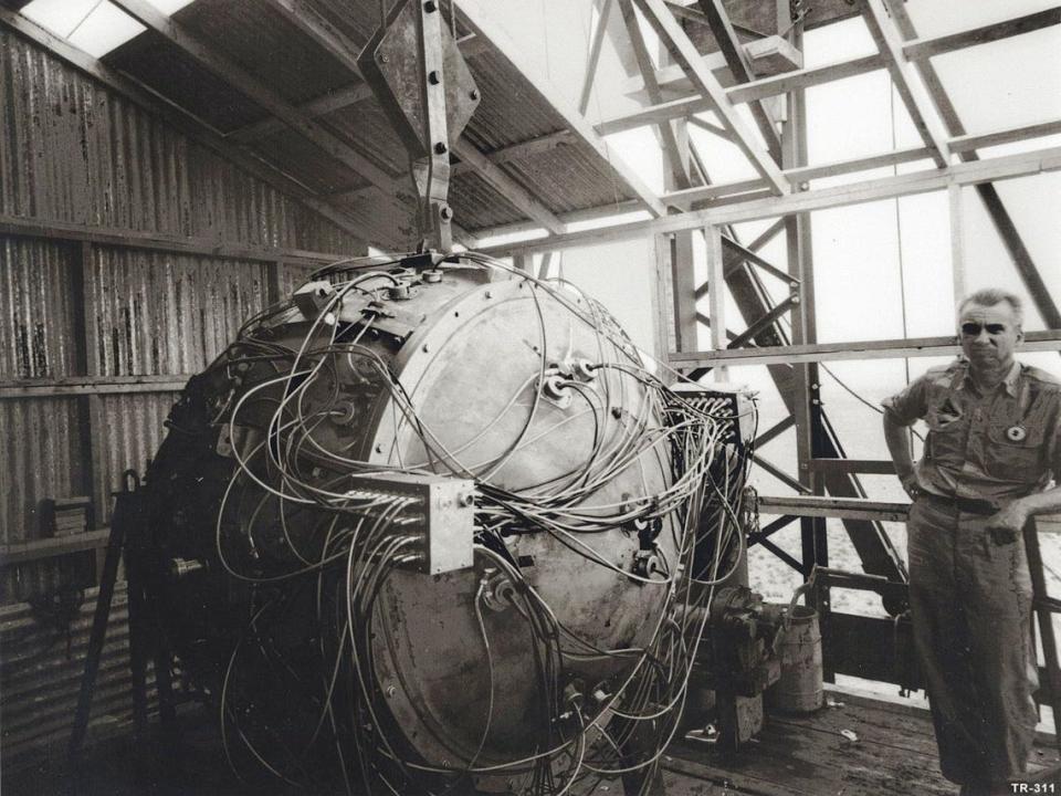 Norris Bradbury stands next to the partially assembled gadget atop the test tower