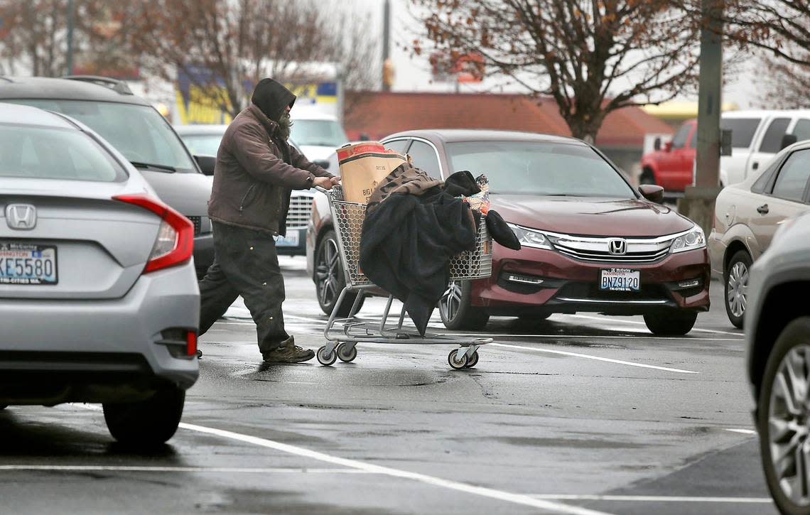 An apparent homeless man pushes his cart filled with his belongings through the Kennewick Plaza shopping area parking lot off Highway 395 and West Kennewick Avenue in Kennewick.