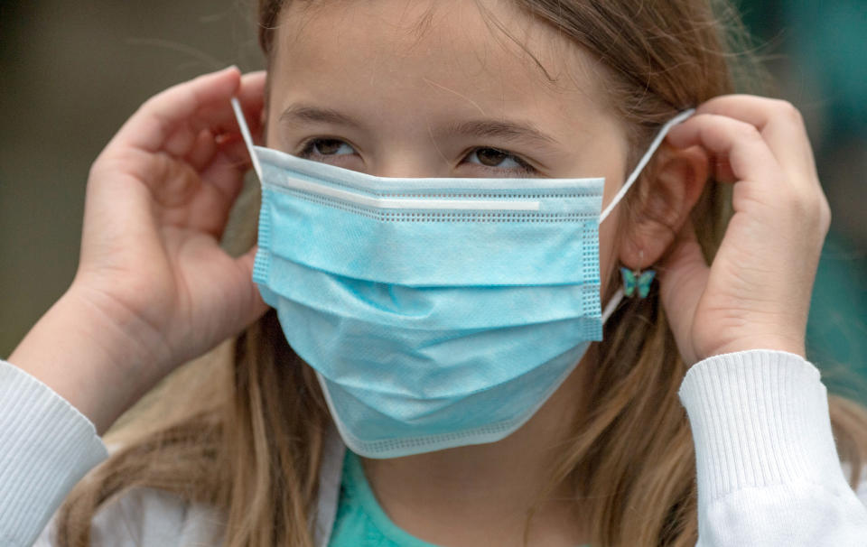 22 June 2020, Hessen, Frankfurt/Main: A primary schoolgirl puts on a disposable mask before entering a school compound. Starting Monday, elementary school children in Hesse will be allowed to come to school together again after months of restrictions. Wearing a mask is no longer mandatory, but is still expressly desired by many schools. Photo: Boris Roessler/dpa (Photo by Boris Roessler/picture alliance via Getty Images)