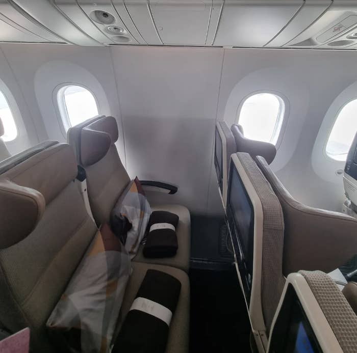 Airplane cabin with empty beige business class seats and folded blankets