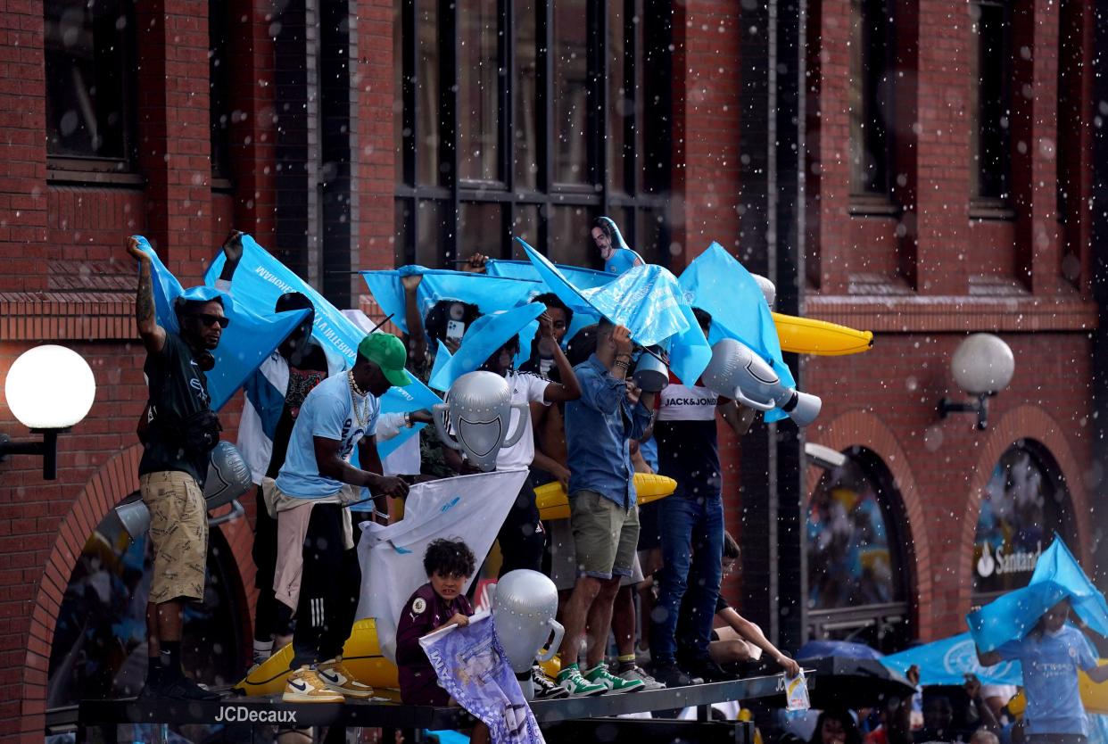 Manchester City fans take shelter from the rain ahead of the Treble Parade in Manchester. (PA)