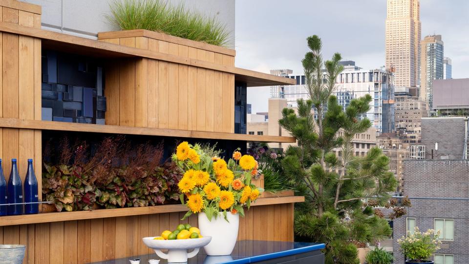 outdoor kitchen counter in blue with yellow flowers in a white vase atop it and the manhattan skyline in the background