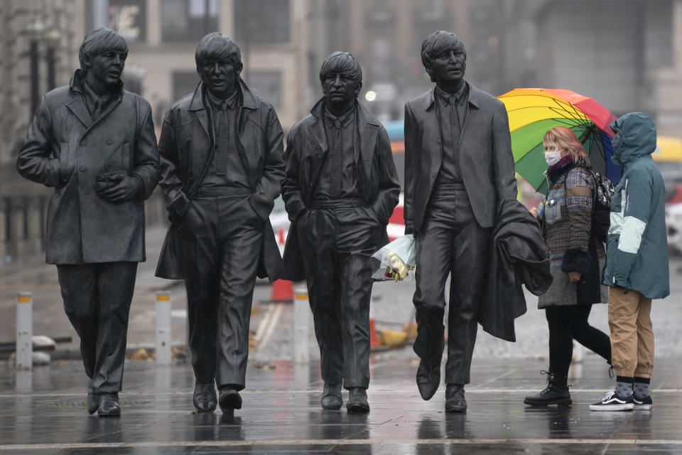 Members of the public wearing face masks stand near a statue of The Beatles in Liverpool, England, Monday Oct. 12, 2020, as Prime Minister Boris Johnson prepares to lay out a new three-tier alert system for England. The Liverpool City Region is expected to face the tightest restrictions under the new system, which will classify regions as being on "medium", "high" or "very high" alert. (AP Photo/Jon Super)