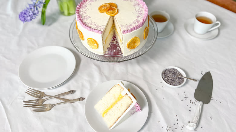 Bright and sunny lemon lavender cake on cake stand with slice cut out on serving plate