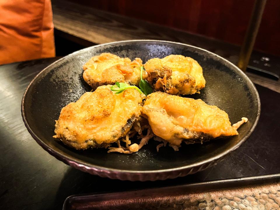 A black bowl with four pieces of golden-brown deep-fried abalone with an herb sprig in the center