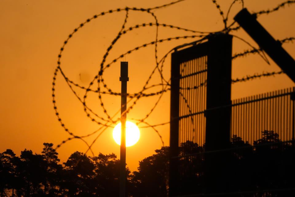 Barbed wir secure the entrance of the harbour area where the landfall of the Nord Stream 1 Baltic Sea pipeline located, as the sun rises behind the pipeline facility and the transfer station of the OPAL gas pipeline, the Baltic Sea Pipeline Link, in Lubmin, Germany, Thursday, July 21, 2022. Europe is bracing for the possibility that the key Nord Stream 1 pipeline that brings natural gas from Russia to Germany won't reopen as scheduled after routine maintenance. (AP Photo/Markus Schreiber)