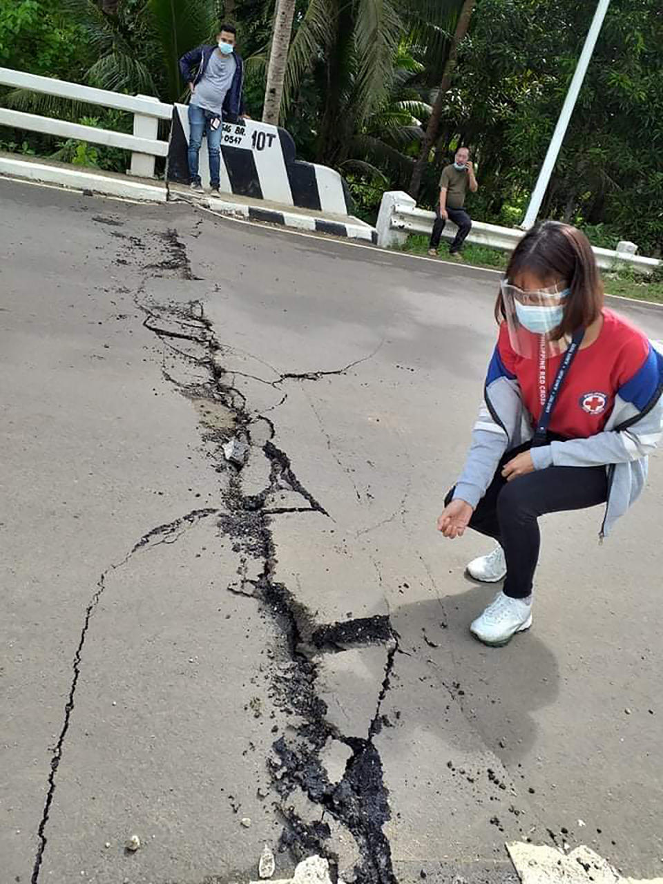 In this photo provided by the Philippine Red Cross, a volunteer looks at the cracks on a road after a quake struck in Cataingan, Masbate province, central Philippines on Tuesday Aug. 18, 2020. A powerful and shallow earthquake struck a central Philippine region Tuesday, prompting people to dash out of homes and offices but there were no immediate reports of injuries or major damage. (John Mark Lalaguna/Philippine National Red Cross via AP)