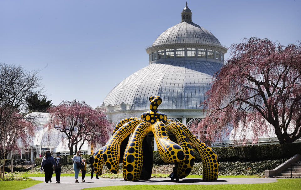 People walk by one of Yayoi Kusama's pumpkin sculptures at the New York Botanical Garden, Thursday, April 8, 2021 in New York. The expansive exhibit has opened, and ticket sales have been brisk in a pandemic-weary city hungry for more outdoor cultural events. (AP Photo/Mark Lennihan)