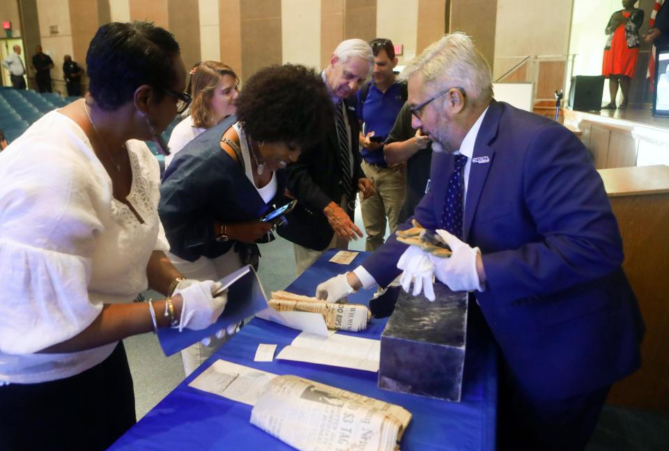 Superintendent Dan Shelton (right), district employees, board members and members of the public examine items found in a 1953 time capsule from the Charles Richard Drew School after it was opened at the Christina School District's board meeting, Tuesday, August 9, 2022.