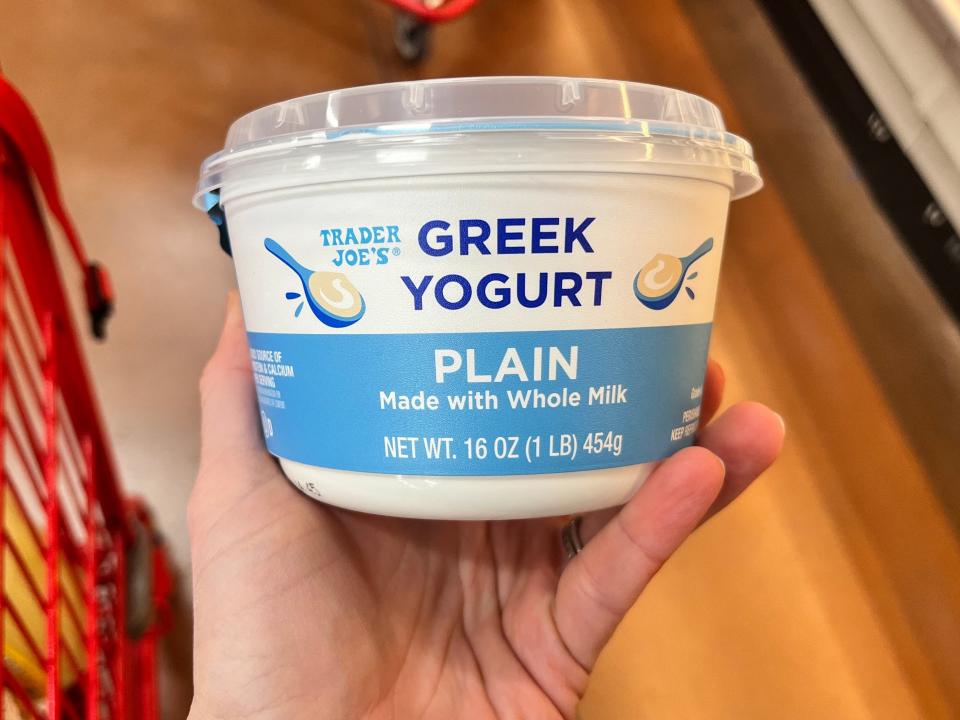 A hand holding a container of Trader Joe's plain Greek yogurt, made with whole milk.