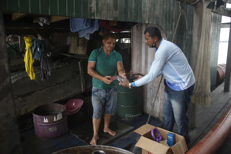 Vendor Leo Goes, 32, right, sells perfume to Illegal gold miner Gerivaldo de Carvalho, 42, on a dredging barge on the Madeira river, a tributary of the Amazon river in Autazes, Amazonas state, Brazil, Thursday, Nov.25, 2021. Hundreds of mining barges have arrived during the past two weeks after rumors of gold spread, with environmentalists sounding the alarm about the unprecedented convergence of boats in the sensitive ecosystem. (AP Photo/Edmar Barros)