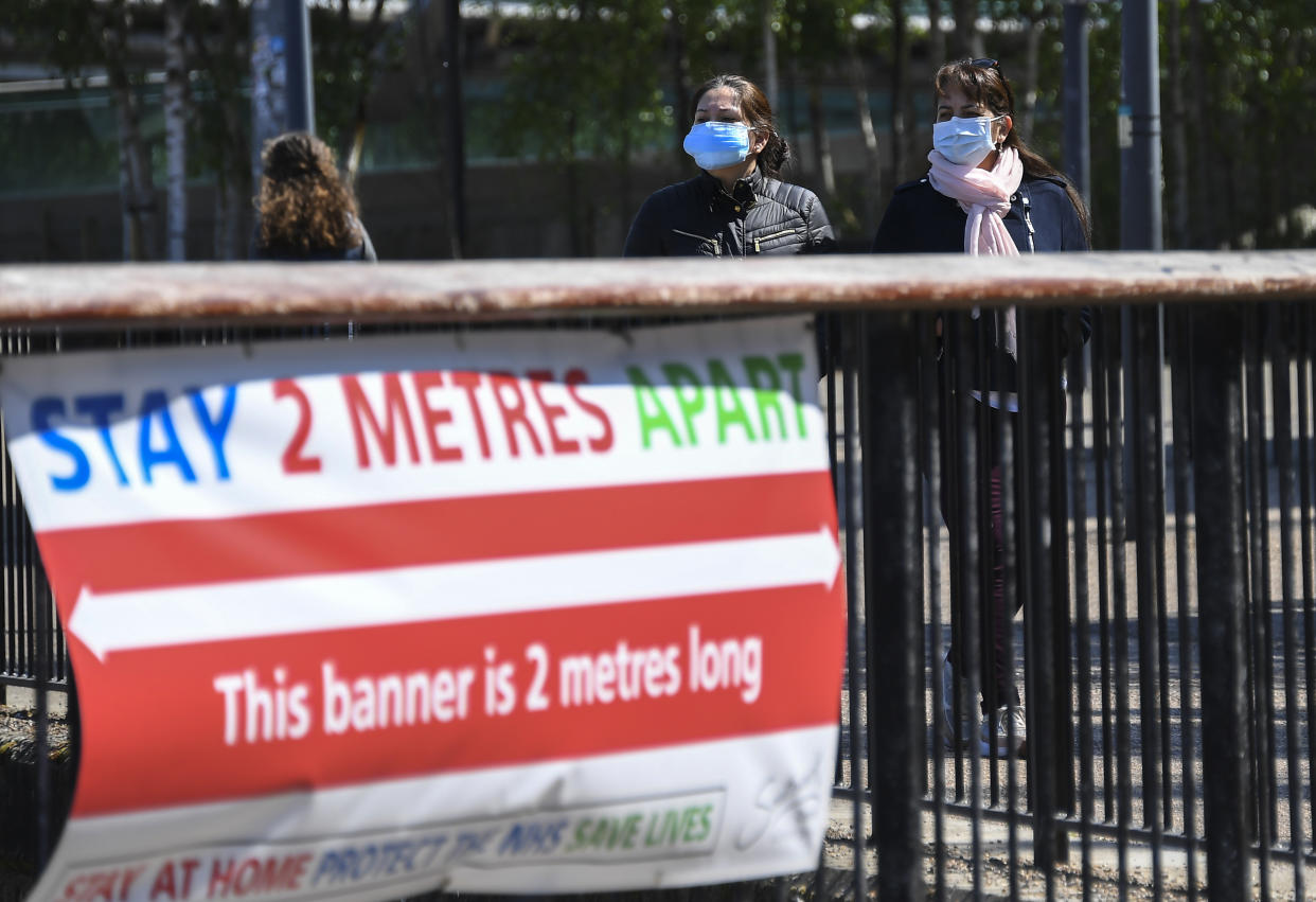 Two women wear protective masks as they walk past a social distancing banner on the south bank of the river Thames, as the lockdown due to the coronavirus outbreak continues, in London, Saturday, April 25, 2020.(AP Photo/Alberto Pezzali)