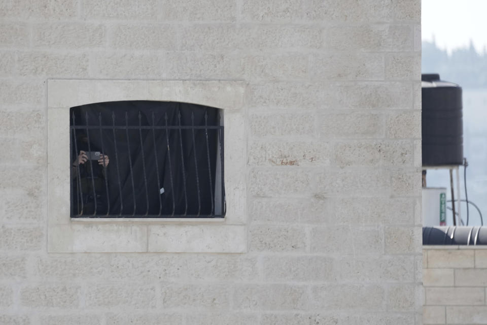 A person films with his mobile phone through a window as Israeli security forces are deployed on the roof of the apartment building of the family of slain Palestinian gunman Uday Tamimi, the village of Anata in east Jerusalem ,Wednesday, Jan. 25, 2023. Israeli forces on Wednesday demolished the home of Tamimi who allegedly killed a female Israeli soldier in an attack last year that sparked a manhunt and clampdown on the east Jerusalem neighborhood where he lived. (AP Photo/ Mahmoud Illean)