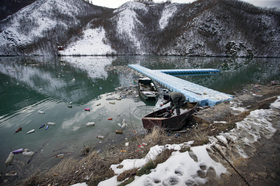 A fisherman prepares his boat at the Potpecko accumulation lake covered with plastic bottles near Priboj, in southwest Serbia, Friday, Jan. 22, 2021. Serbia and other Balkan nations are virtually drowning in communal waste after decades of neglect and lack of efficient waste-management policies in the countries aspiring to join the European Union. (AP Photo/Darko Vojinovic)