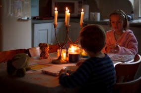 Image shows a young boy and girl sitting at the table eating breakfast. The room is lit by candles because there has been a powe