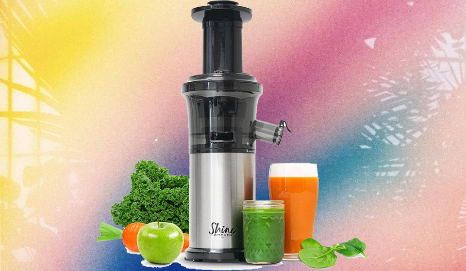 A juicer with kale, apples next to two containers of juice on a tropical background