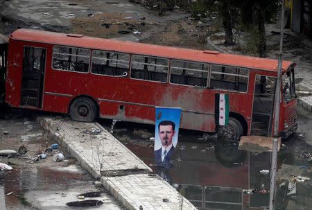 FILE PHOTO: A picture of Syrian President Bashar al-Assad is seen near a Syrian opposition flag in Aleppo's Bustan al-Basha district, in Syria December 3, 2013. REUTERS/Molhem Barakat/File Photo