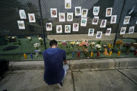 Leo Soto, who created this memorial with grocery stores donating flowers and candles, pauses in front of photos of some of the missing people that he put on a fence, near the site of an oceanfront condo building that partially collapsed in Surfside, Fla., Friday, June 25, 2021. (AP Photo/Gerald Herbert)