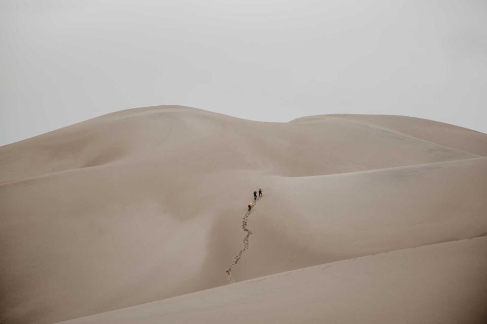 Three people trek up sand dunes near Zapata Ranch in Southern Colorado