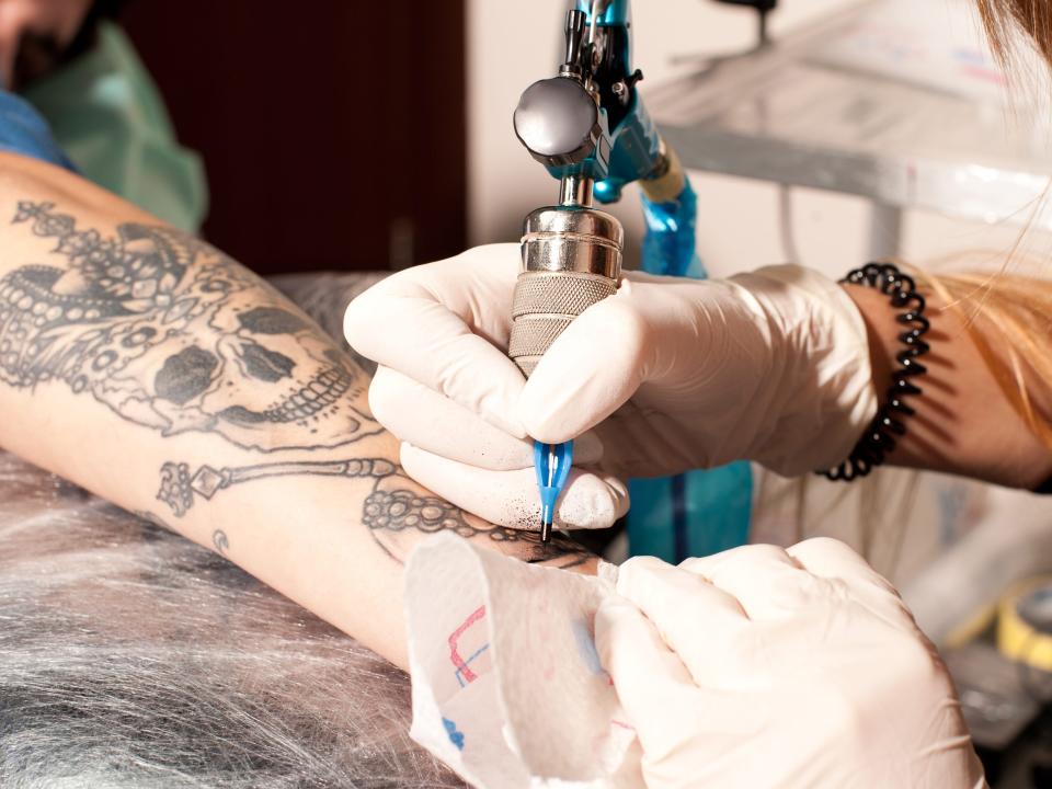 someone tattooing a skeleton with crown jewels onto someone's forearm