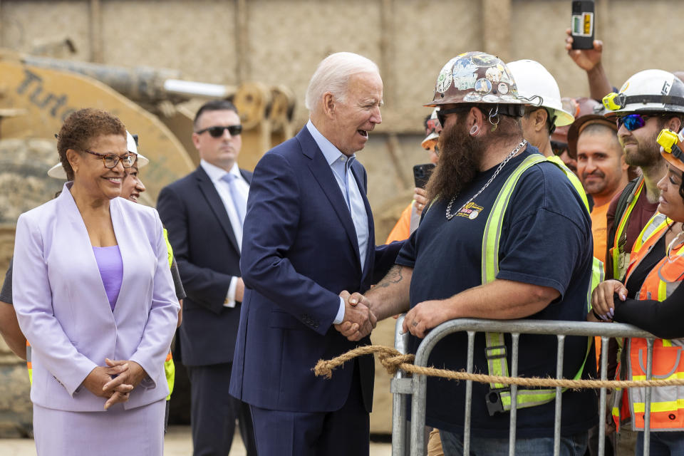 FILE - President Joe Biden, center, greets with Kevin Corbin, a union heavy equipment operator at the LA Metro, D Line Extension Transit Project - Section 3, as Biden arrives to speak about infrastructure investments at the LA Metro, D Line (Purple, File) Extension Transit Project - Section 3, in Los Angeles, Thursday, Oct. 13, 2022. Rep. Karen Bass, D-Calif., looks on at left. (AP Photo/Alex Gallardo, File)