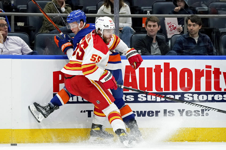 Calgary Flames defenseman Noah Hanifin (55) pins New York Islanders left wing Anthony Beauvillier (18) against the boards during the second period of an NHL hockey game, Monday, Nov. 7, 2022, in Elmont, N.Y. (AP Photo/Julia Nikhinson)