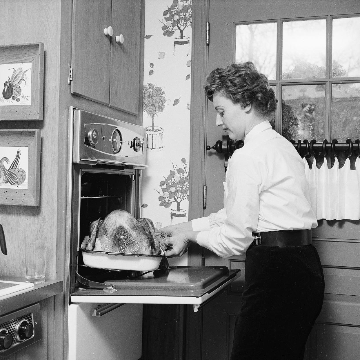 1950's woman checking on her turkey in the oven